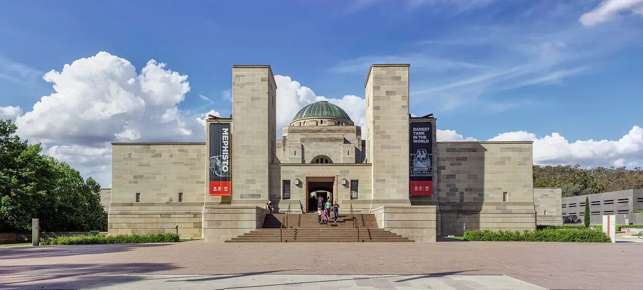 ด้านหน้าอาคาร Australian War Memorial ที่มีโดมสีเขียวและป้ายนิทรรศการสองข้างบันไดทางเข้า ภาพพาโนรามาจาก Wikimedia Commons ผู้ถ่าย Thennicke สัญญา CC BY-SA 4.0 ไม่ระบุปีที่ถ่าย
