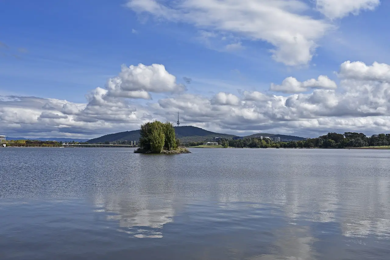 ผิวน้ำของทะเลสาบ Burley Griffin มีเกาะเล็ก ๆ กลางน้ำและเนินเขากับเสาสูงไกล ๆ ภาพจาก Wikimedia Commons ผู้ถ่าย Ymblanter สัญญา CC BY-SA 4.0 ไม่ระบุปีที่ถ่าย