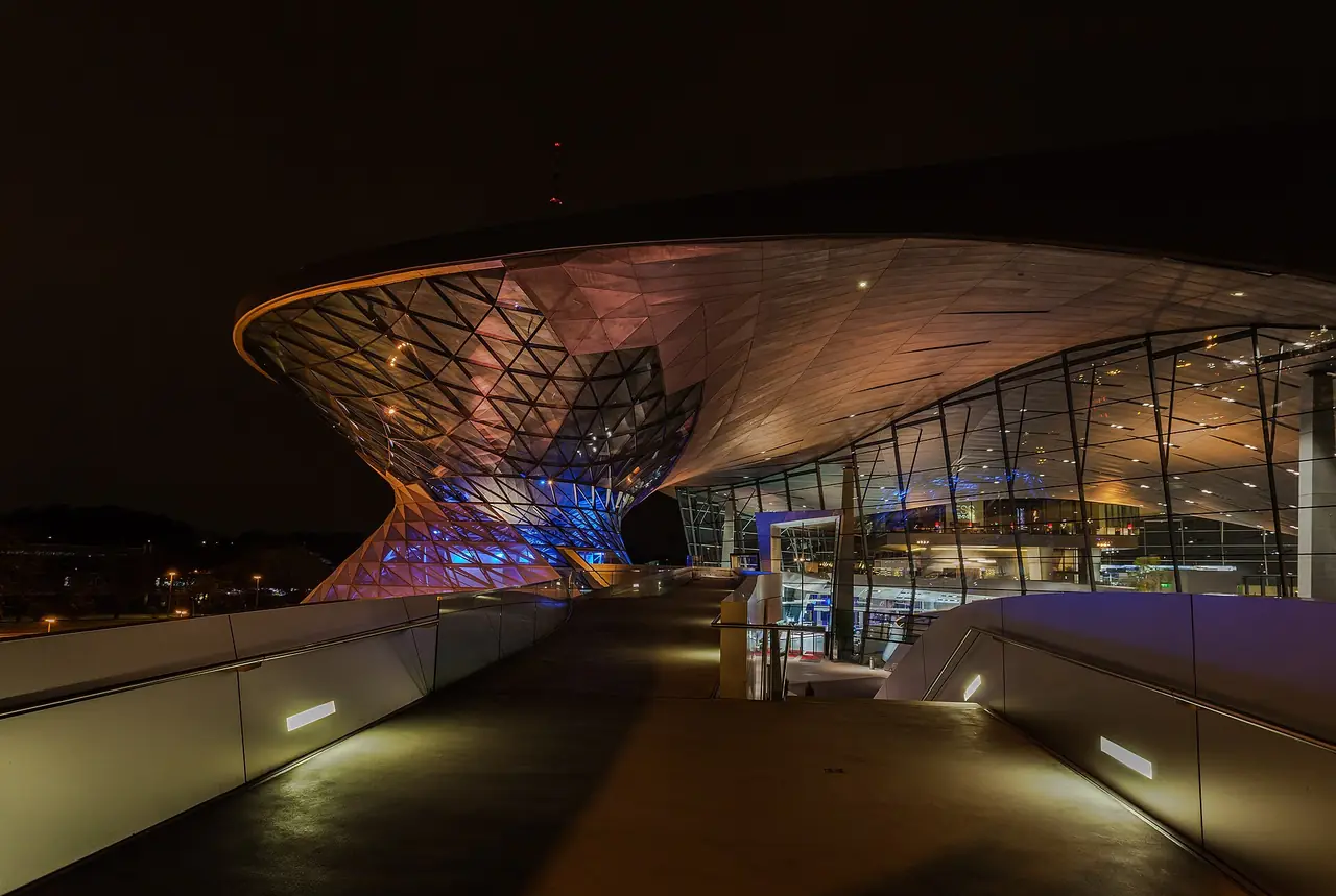 โครงสร้างกรวยคู่ของ BMW Welt ยามค่ำ มองจากสะพานทางเข้า ภาพจาก Wikimedia Commons ผู้ถ่าย Diego Delso สัญญา CC BY-SA 3.0 ถ่ายปี 2556