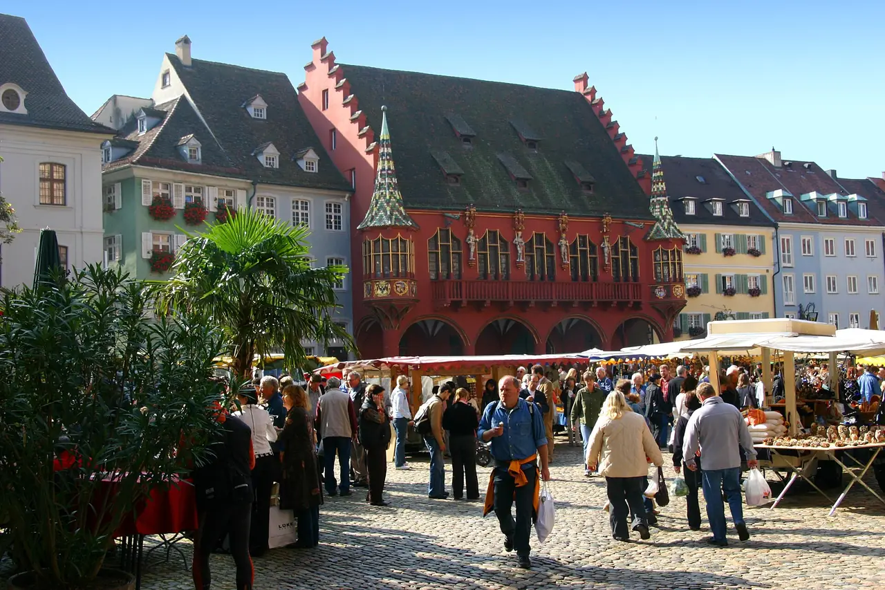 ตลาด Münsterplatz หน้าอาคาร Historisches Kaufhaus สีแดง ภาพจาก Wikimedia Commons ผู้ถ่าย Gerd Eichmann สัญญา CC BY-SA 4.0 ถ่ายปี 2550