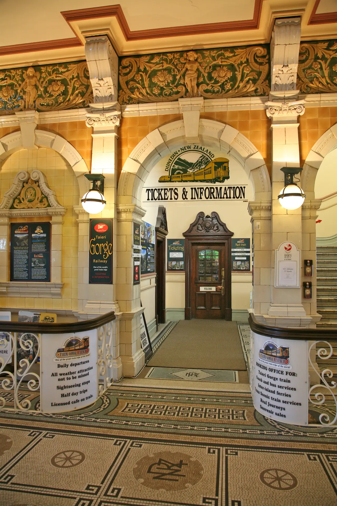 ห้องโถงจองตั๋วภายในสถานีรถไฟ Dunedin พื้นโมเสกและป้าย Tickets and Information ภาพจาก Wikimedia Commons ผู้ถ่าย W. Bulach สัญญา CC BY-SA 4.0 ไม่ระบุปีที่ถ่าย ป้ายในภาพอาจไม่ตรงกับปัจจุบัน