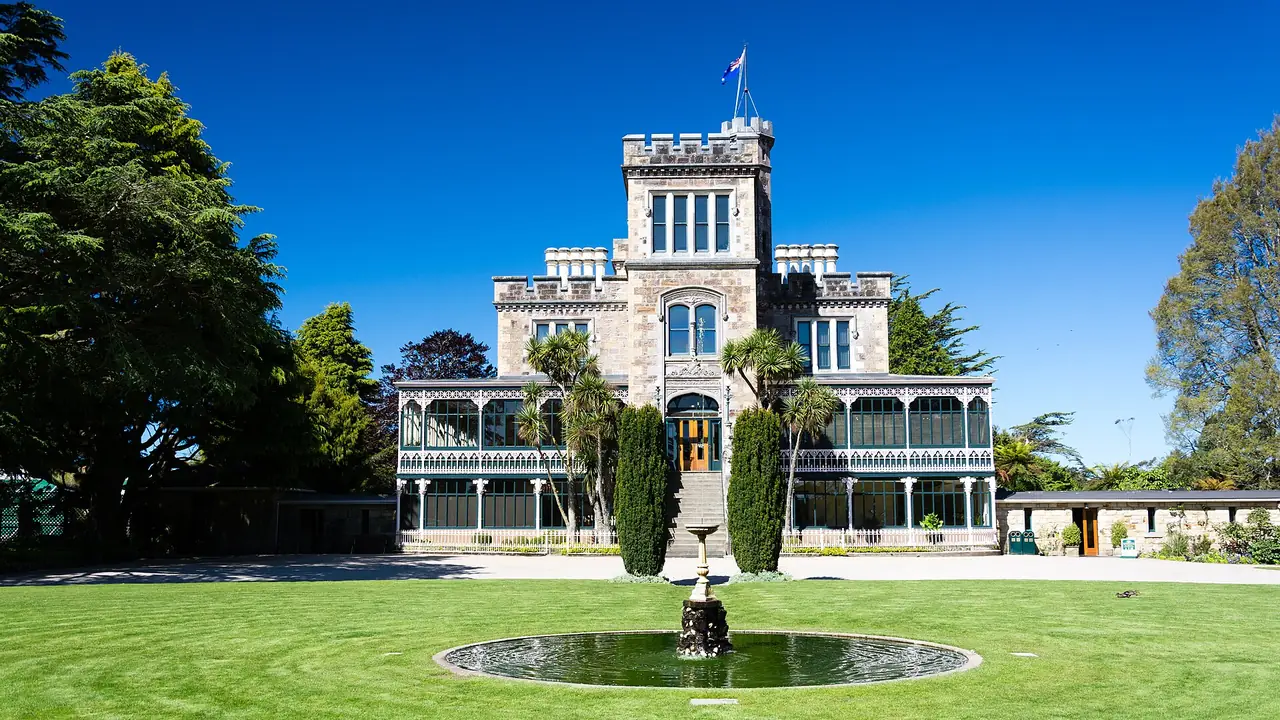 ปราสาท Larnach มองจากสนามหญ้าและน้ำพุหน้าอาคาร ภาพจาก Wikimedia Commons ผู้ถ่าย Christoph Strässler สัญญา CC BY-SA 2.0 ไม่ระบุปีที่ถ่าย