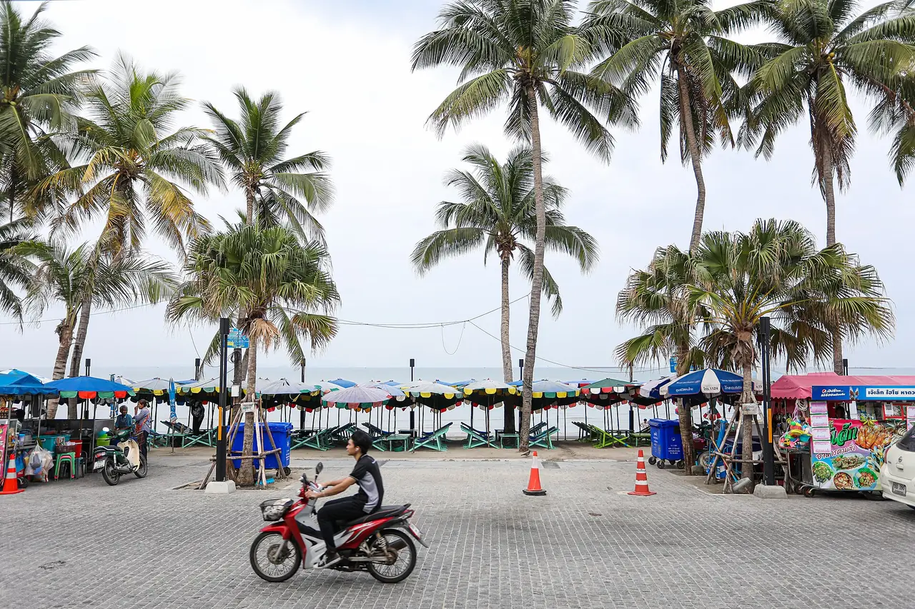 ถนนริมหาดบางแสนล่าง ร้านขายของและเก้าอี้ผ้าใบเรียงริมทะเล มีมอเตอร์ไซค์วิ่งผ่าน ภาพจาก Wikimedia Commons ผู้ถ่าย Adirach Toumlamoon สัญญา CC BY-SA 4.0 ไม่ระบุปีที่ถ่าย
