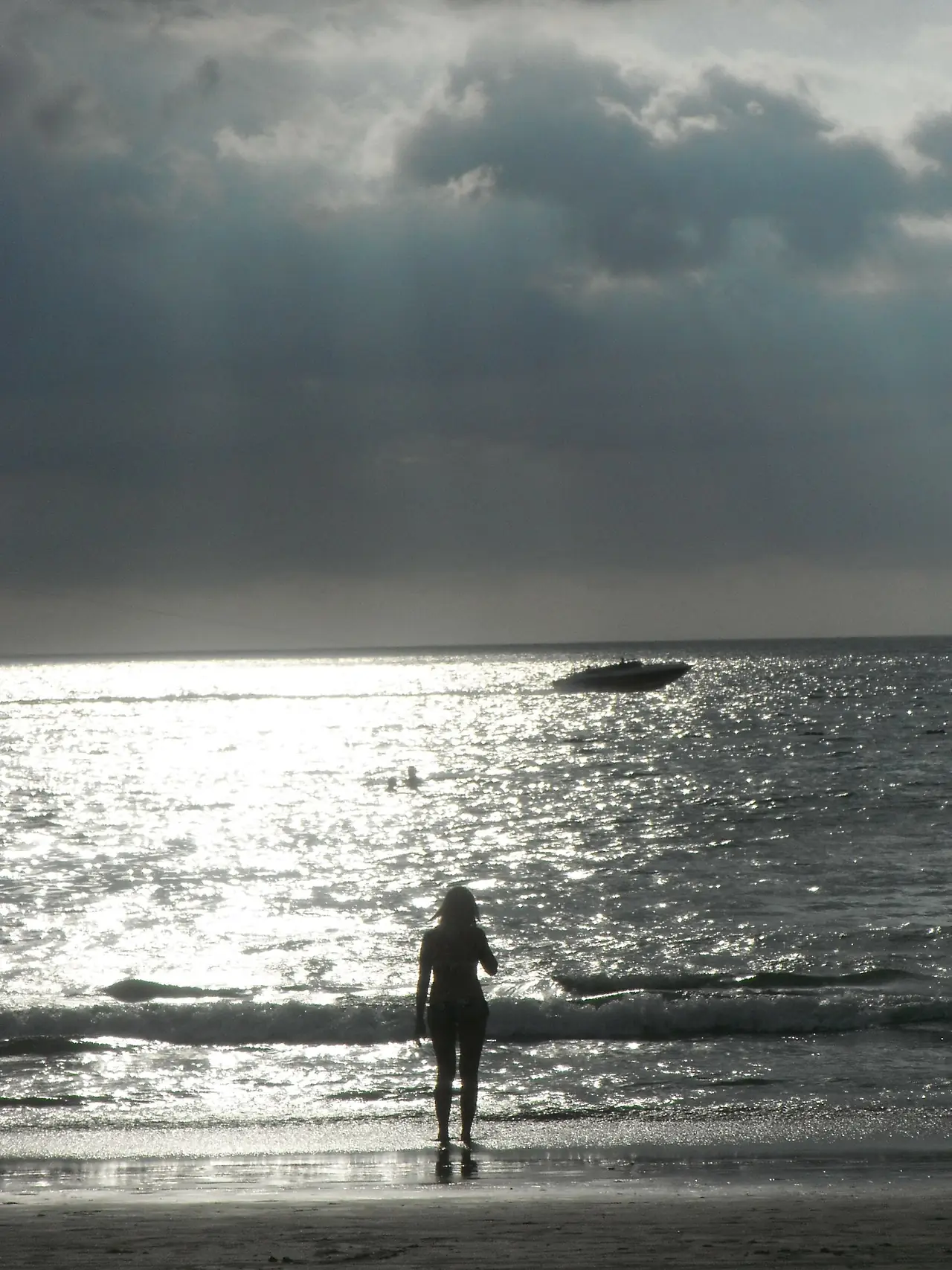 ผู้หญิงยืนที่ชายหาดป่าตองมองทะเลสะท้อนแสงขณะเมฆฝนเข้า มีเรือเร็วลอยอยู่ไกล ภาพจาก Wikimedia Commons ผู้ถ่าย Paul IJpelaar สัญญา CC BY 3.0 ตามชื่อไฟล์คือพายุกำลังเข้า ไม่ระบุปีที่ถ่าย
