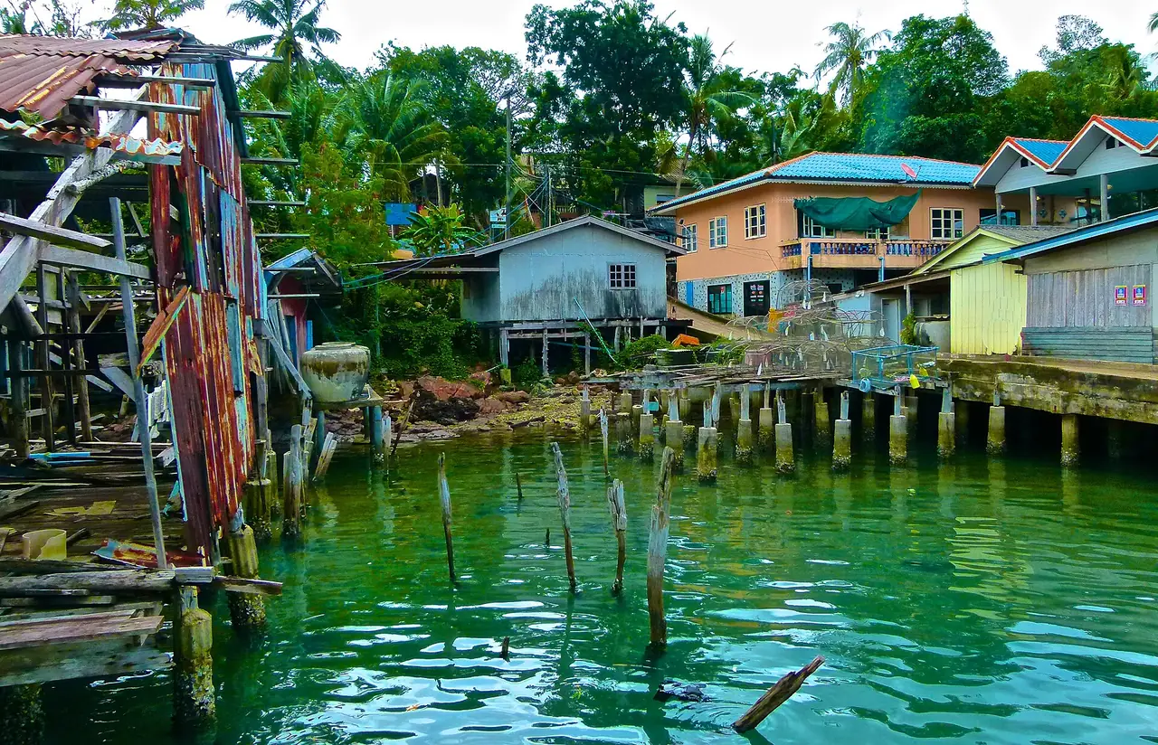 บ้านเรือนริมน้ำ สะพานปูน และเสาไม้เก่าของหมู่บ้านอ่าวสลัด เกาะกูด ภาพจาก Wikimedia Commons ผู้ถ่าย josef knecht สัญญา CC BY 3.0 ตามชื่อไฟล์บน Commons เป็นภาพหมู่บ้านอ่าวสลัด ไม่ระบุปีถ่าย อาจเก่า