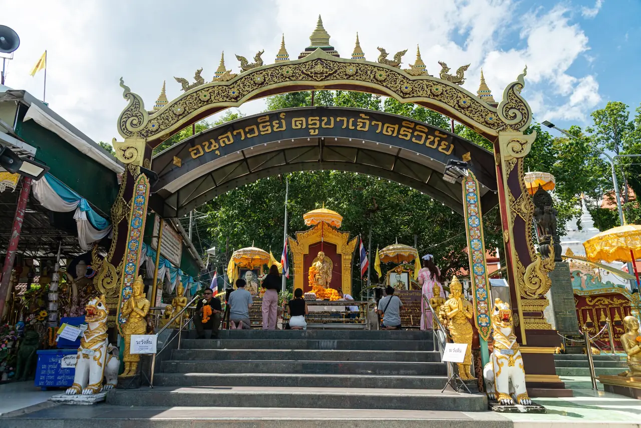 ซุ้มประตูทองชื่ออนุสาวรีย์ครูบาเจ้าศรีวิชัย มีบันไดและรูปปั้นสิงห์ ผู้คนกราบไหว้ด้านใน ภาพจาก Wikimedia Commons ผู้ถ่าย Kimtuy สัญญา CC BY-SA 4.0 ถ่ายเดือนพฤษภาคม 2564 ที่จุดเริ่มถนนขึ้นดอยสุเทพ จังหวัดเชียงใหม่ เป็นอนุสาวรีย์ของครูบาอีกรูปคนละที่กับห้วยต้ม ใช้ประกอบเรื่องการเคารพครูบาในล้านนา