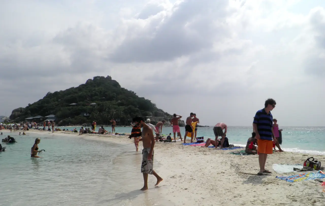 หาดทรายนวลของเกาะนางยวนช่วงที่คนพลุกพล่าน มีเนินป่าอยู่ด้านหลัง ภาพของ Hmaglione10 จาก Wikimedia Commons สัญญา CC BY-SA 4.0