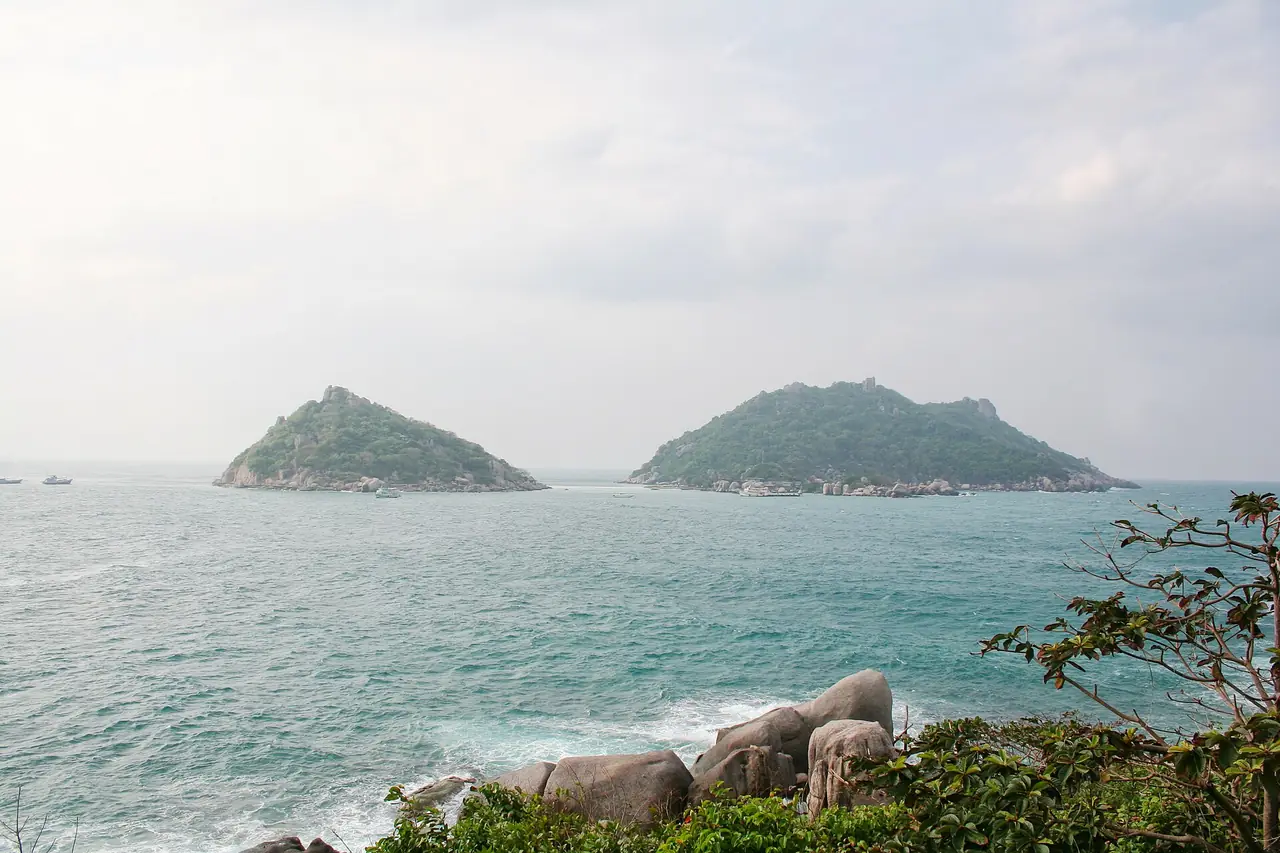 เกาะหินป่าสองลูกมองข้ามน้ำจากแหลมหินริมทะเล ภาพที่ Commons ระบุว่าเป็นเกาะนางยวน ถ่ายจากฝั่งไกลออกมา เราไม่ยืนยันจุดถ่ายที่แน่ชัด ภาพจาก Wikimedia Commons ผู้ใช้นามแฝง สัญญา CC0