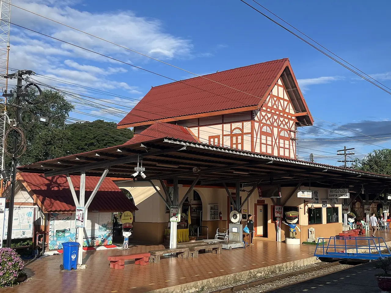 อาคารสถานีรถไฟบ้านปินสองชั้น ชั้นบนเป็นไม้โครงเปิดสีส้มแบบบาวาเรีย หลังคาแดง ภาพจาก Wikimedia Commons ผู้ถ่าย Tealsp สัญญา CC BY-SA 4.0 ไม่ระบุวันที่ถ่าย