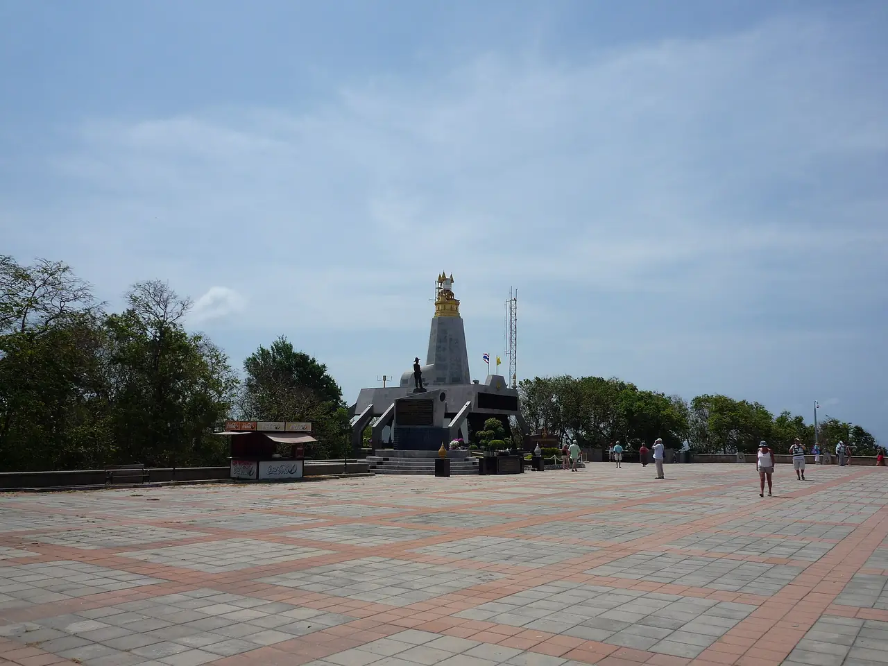 ลานปูกระเบื้องหน้าประภาคารแหลมพรหมเทพ มีหอสีขาวยอดทอง มีรูปปั้นหน้าหอ ร้านเล็กหนึ่งร้านทางซ้าย และคนเดินกระจายบนลาน ภาพจาก Wikimedia Commons ผู้ถ่าย ADwarf สัญญา สาธารณสมบัติ ไม่ระบุปีที่ถ่ายในไฟล์ เป็นภาพประกอบ ร้านและลานอาจเปลี่ยนไปแล้ว